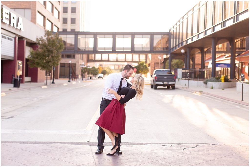 Engaged couple in formal outfit doing a dip kiss in the middle of a downtown street.